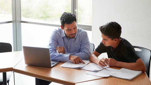 A tutor helps a teen boy with a workbook assignment