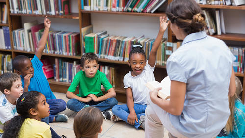 kids sitting on a floor in library and listening the teacher