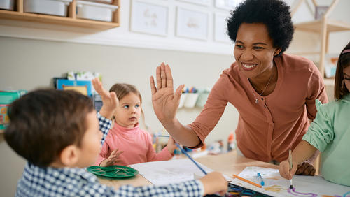 Happy African American teacher and small boy giving high-five during art class at kindergarten