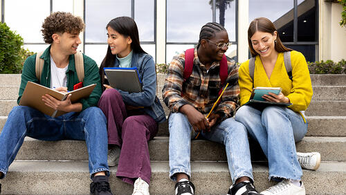 group of four students are sitting on the stairs ourside of college building