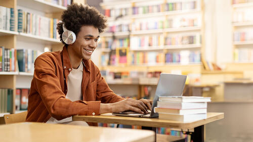 young men smiling while looking at laptop in library