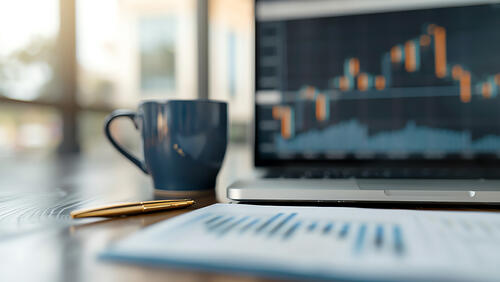a cup in front of open laptop with graphs on a screen