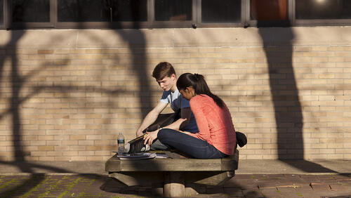 Two college students studying on a campus bench 