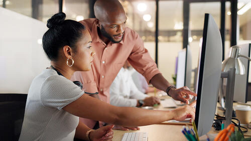 a man is helping a yong women, showing something on computer monitor