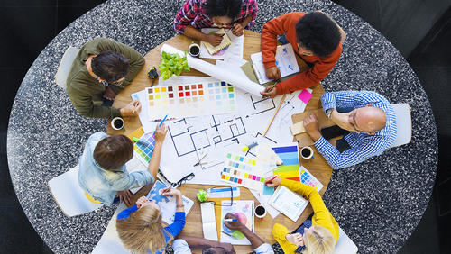 a group of coworkers sitting at a round table, shown from overhead, collaborating on a project 