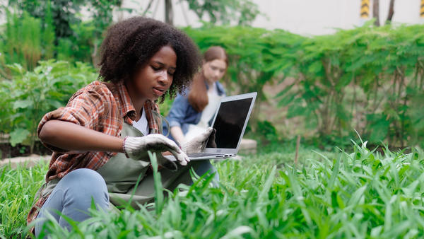 Two high school students in a garden, checking information on a laptop