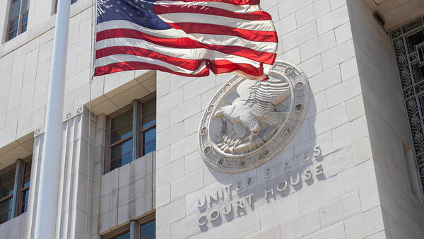American flag waving in front of a building with a plaque that reads United States Court House