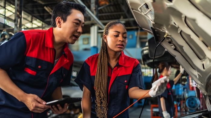 Male instructor helps female student with car repair