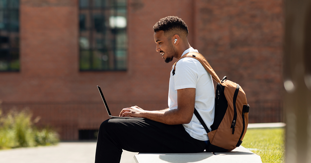 a young men sitting on a banch with a laptop