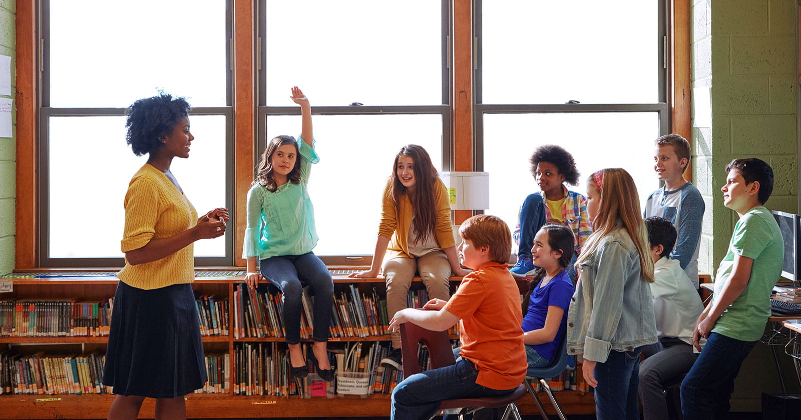 A teacher instructs a diverse group of middle school students in a library.