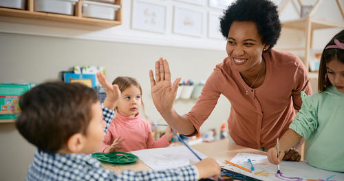 Happy African American teacher and small boy giving high-five during art class at kindergarten