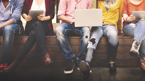 Group of young adults sitting in a row using laptops