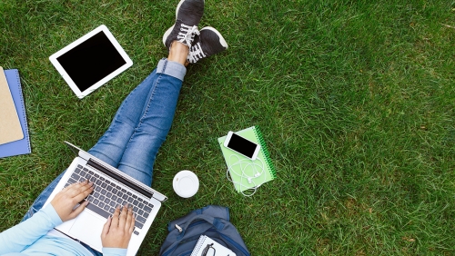Student studying in a park, surrounded by books and mobile devices