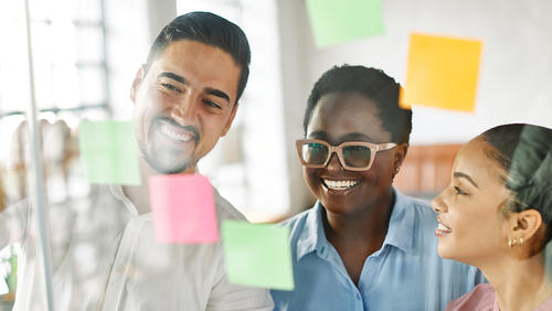 three people putting ideas on sticky notes