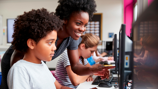 Black teacher assisting young black student with a computer