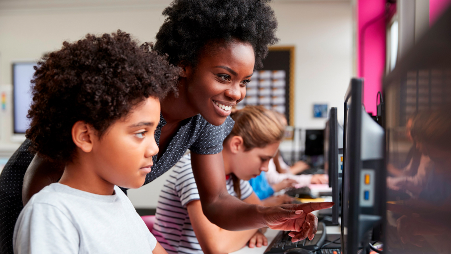 Black female teacher assisting young black student with a computer